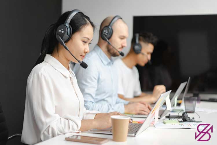 تصویر افرادی که هدفون به گوش دارند و در کنار یکدیگر نشسته و مشغول کار با لپتاپ هستند و گویی تیم پشتیبانی میلی گلد باشند 